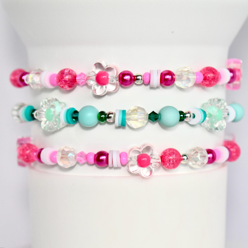 Three pink, turquoise, and white beaded bracelets with flower charms. The bracelets are stacked on top of each other.