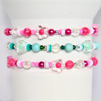 Three pink, turquoise, and white beaded bracelets with flower charms. The bracelets are stacked on top of each other.