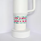 A white tumbler with a stack of colorful beaded bracelets. The bracelets are made of pink, green, blue, and clear beads.