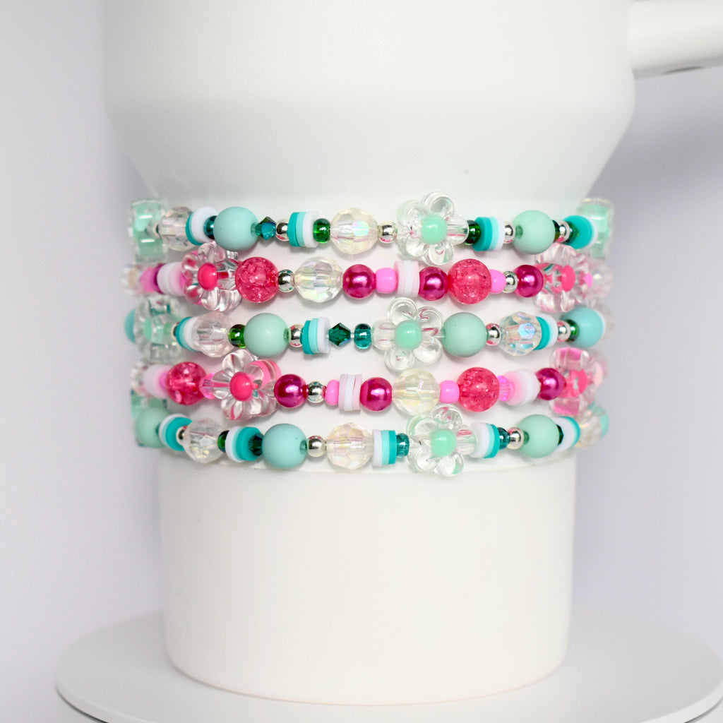 Mint green and hot pink tumbler bracelet set with flower charms, crystal beads, and striped accents, wrapped around a white tumbler.