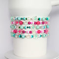 Mint green and hot pink tumbler bracelet set with flower charms, crystal beads, and striped accents, wrapped around a white tumbler.
