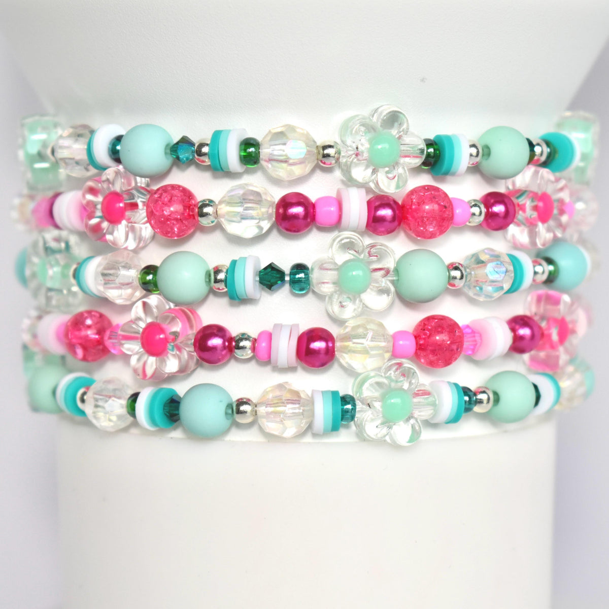 A multi-strand bracelet with pink, green, and white beads. The bracelet features flower-shaped beads and clear crystal beads.