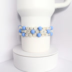 A triple strand bracelet with blue and white beads. The bracelet is made of light blue matte beads, white pearl beads, and iridescent clear beads.