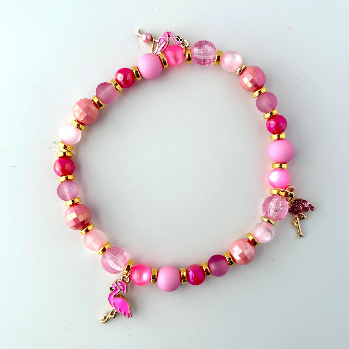 A pink beaded bracelet with three pink flamingo charms. The bracelet is made with pink and gold beads.