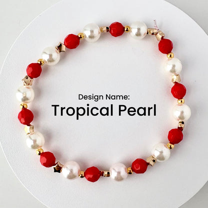 A beaded bracelet with the text "Tropical Pearl." The bracelet features alternating white pearl beads and red faceted beads, with gold-colored star and round accents.