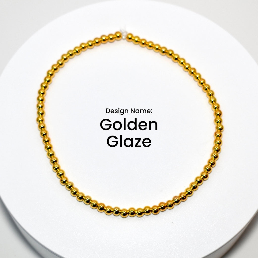 A gold beaded bracelet with a simple design. The bracelet is on a white surface. Design Name: Golden Glaze