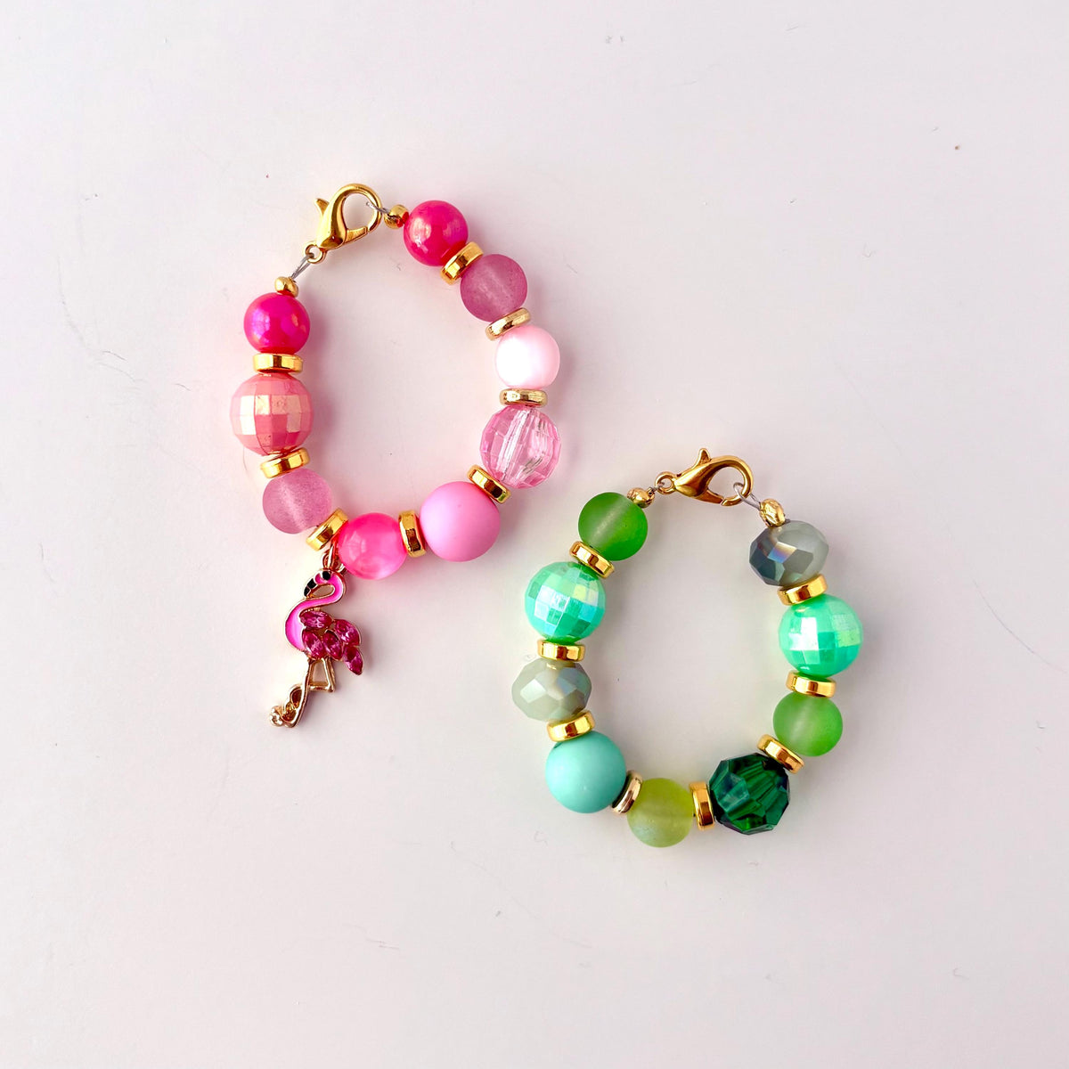 Two beaded tumbler handle bracelets, one pink and one green. The pink bracelet has a flamingo charm. Both bracelets have gold lobster clasps.