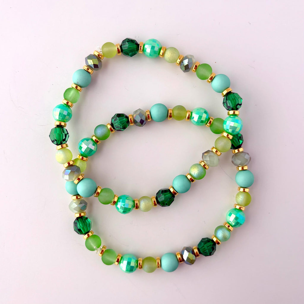 Two green and gold beaded bracelets with light blue, green, and gold beads. The bracelets are stacked on top of each other.