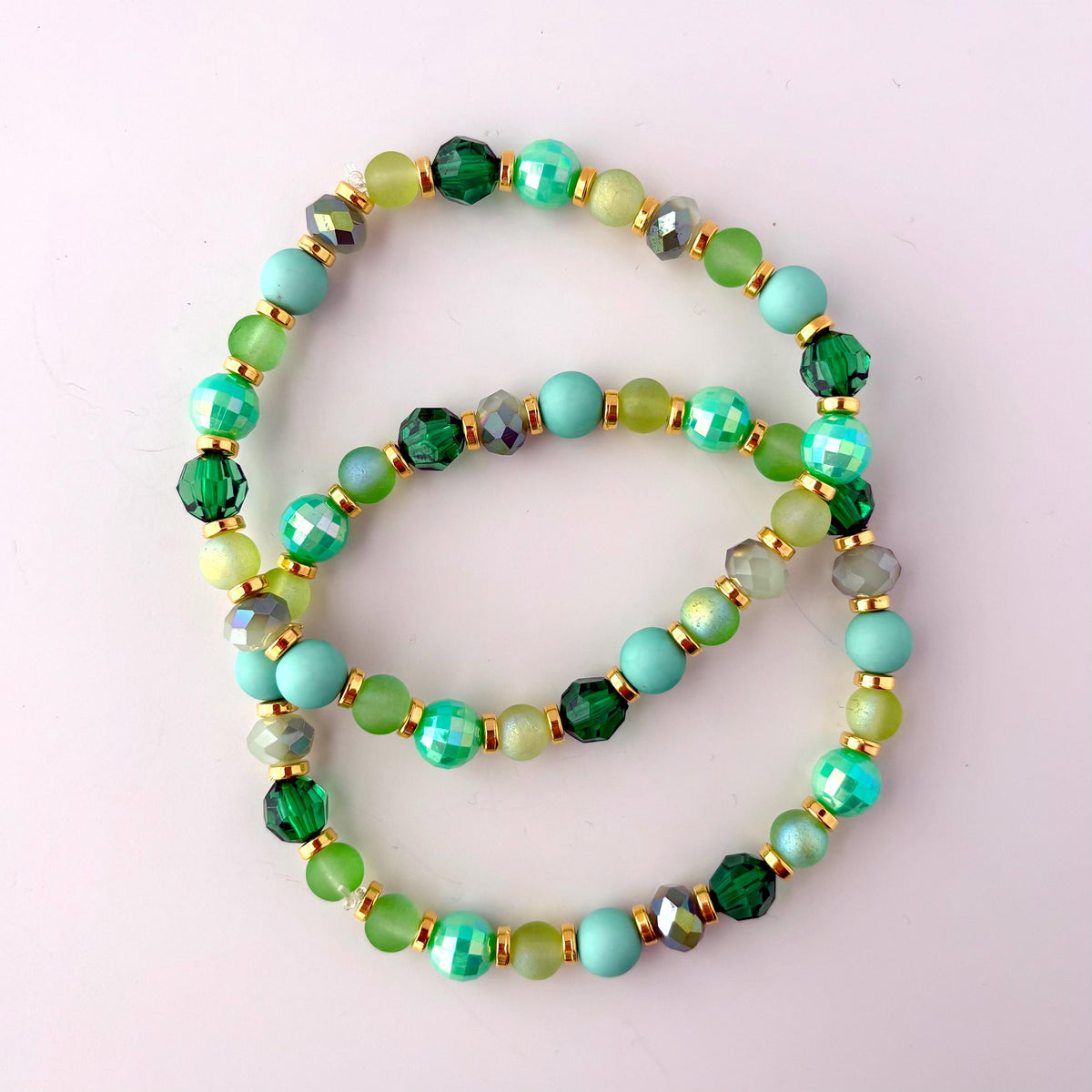 Two green and gold beaded bracelets with light blue, green, and gold beads. The bracelets are stacked on top of each other.