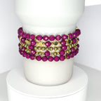 Handmade tumbler bracelet set featuring faceted magenta beads and shiny gold accents, stacked around a white tumbler for a stylish, elegant look.