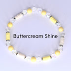 A beaded bracelet with the text "Buttercream Shine". The bracelet features a mix of yellow, white, and clear beads. The beads are arranged in a circular pattern, creating a stylish accessory.