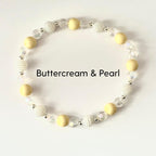 A beaded bracelet featuring a mix of creamy yellow and pearl-like beads. The bracelet includes round, matte yellow beads, textured white beads, and clear, faceted beads. The text "Buttercream & Pearl" is displayed.