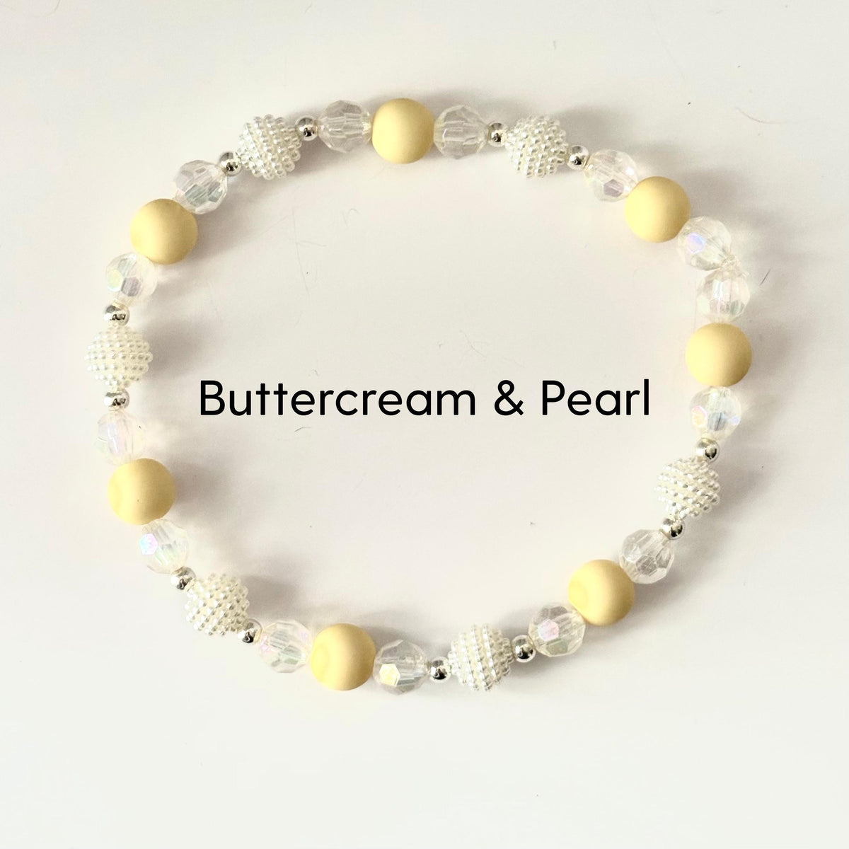 A beaded bracelet featuring a mix of creamy yellow and pearl-like beads. The bracelet includes round, matte yellow beads, textured white beads, and clear, faceted beads. The text "Buttercream & Pearl" is displayed.