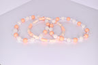A trio of tumbler bracelets arranged in an overlapping display on a white surface, featuring a mix of peach matte beads, clear faceted beads, textured white pearl beads, and flat cream and peach disc beads in complementary patterns.