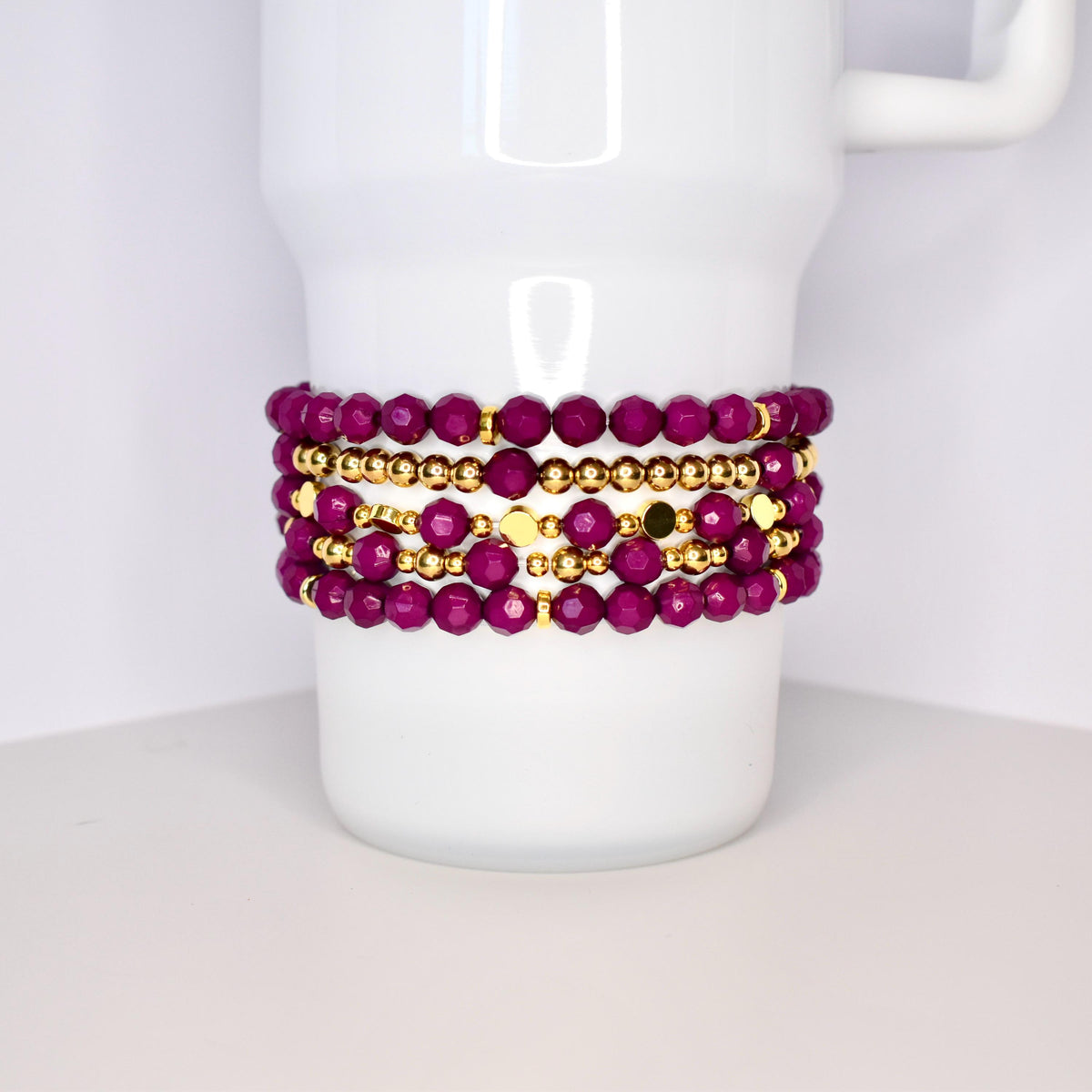 A set of five bracelets featuring a mix of deep purple and gold beads. The bracelets are stacked on top of each other, creating a layered look.