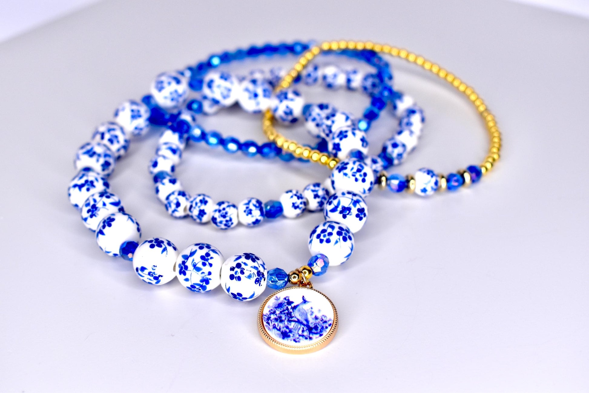 Four blue and white beaded bracelets with a blue and white floral charm. The bracelets are made of small, round beads with a floral pattern. The charm is a round, flat disc with a floral design.
