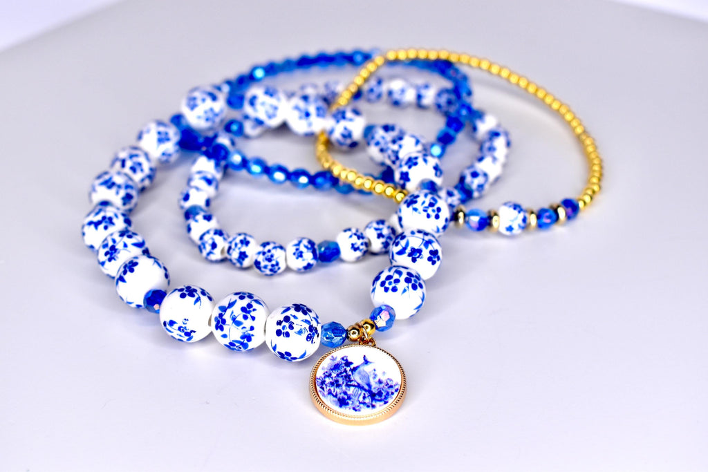 Four blue and white beaded bracelets with a blue and white floral charm. The bracelets are made of small, round beads with a floral pattern. The charm is a round, flat disc with a floral design.