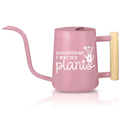 A light pink watering can with a wooden handle. The watering can has a spout and a white inscription that reads 'sometimes i wet my plants' with a small flower and watering can graphic.