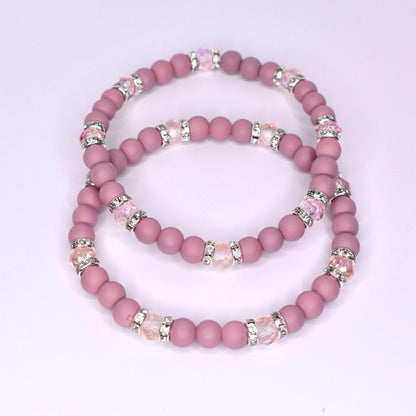 Two beaded bracelets in a dusty rose color. Each bracelet features small, round beads and sections of larger, clear beads with silver accents. The bracelets are stacked together, showcasing their similar design and color palette.