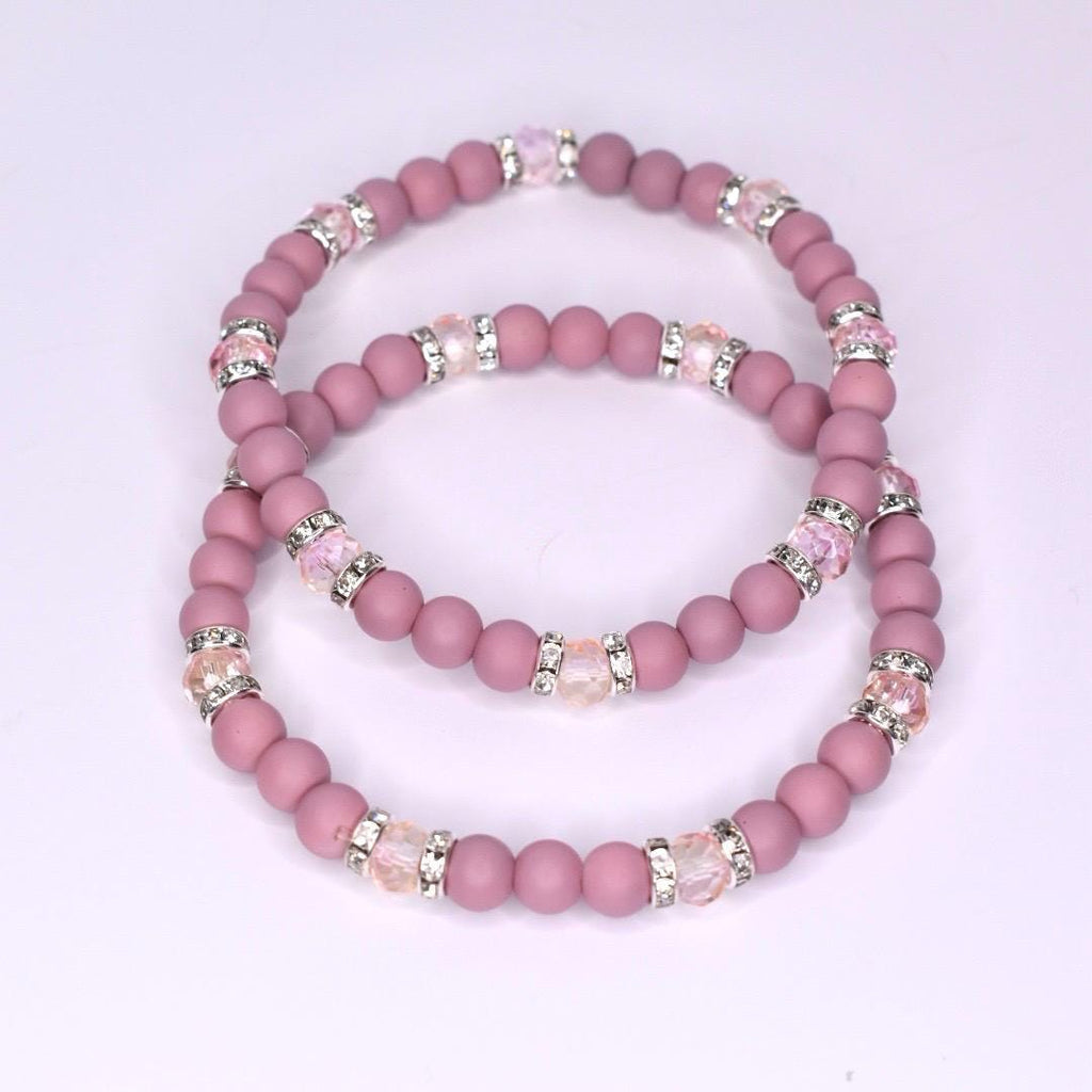 Two beaded bracelets in a dusty rose color. Each bracelet features small, round beads and sections of larger, clear beads with silver accents. The bracelets are stacked together, showcasing their similar design and color palette.