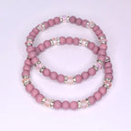 Two beaded bracelets in a dusty rose color. Each bracelet features small, round beads and sections of larger, clear beads with silver accents. The bracelets are stacked together, showcasing their similar design and color palette.