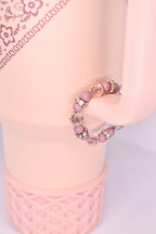 A beaded tumbler handle bracelet with a pink and clear color scheme. The ring features small, round pink beads interspersed with larger, faceted clear beads. Silver-colored, decorative accents are placed between some of the beads. The ring is displayed on a light pink surface.