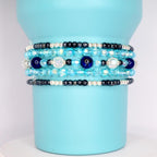 Close-up of multi-layer tumbler bracelets with glass beads in ocean tones, adding a stylish grip to a blue insulated tumbler.