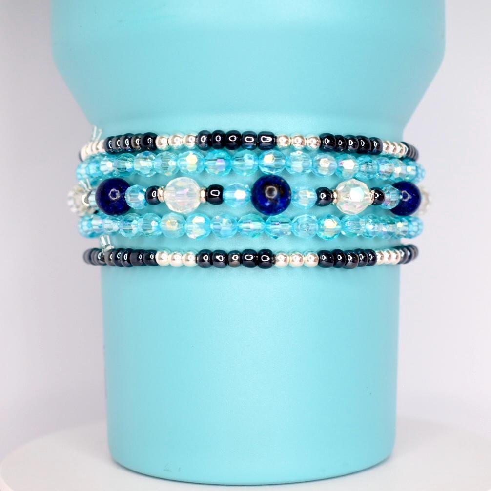 Close-up of multi-layer tumbler bracelets with glass beads in ocean tones, adding a stylish grip to a blue insulated tumbler.