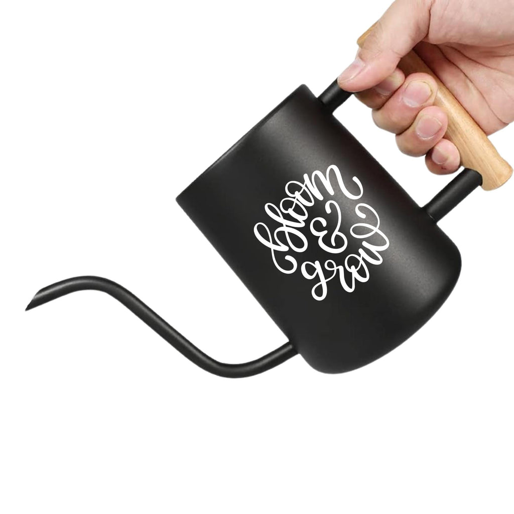 A black gooseneck kettle with a wooden handle and the words "bloom & grow" in white script. The kettle is designed for precise pouring and has a long, slender spout. Ideal for brewing coffee or tea.
