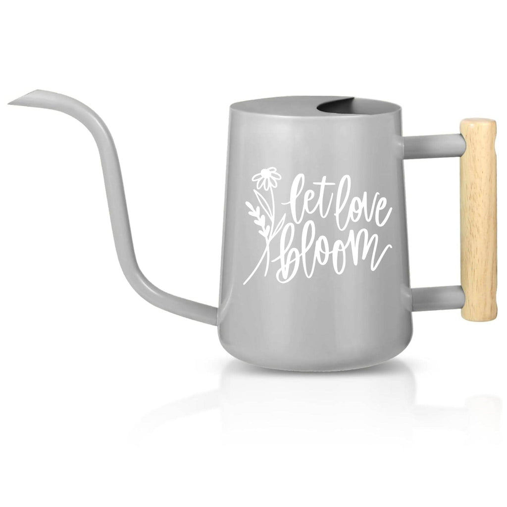 A gray watering can with a long, curved spout and a wooden handle. The watering can features the words 'let love bloom' in white script. The handle is a light brown color. The watering can is designed for gardening and plant care.