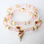 Three beaded bracelets in shades of pink and white. The bracelets feature a mix of pink faceted beads, white pearl-like beads, and gold-colored accents. One bracelet has a heart-shaped pendant with a floral design and a dangling crystal.