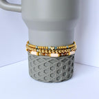 Sage and gold tumbler bracelet set with three stretch beaded cup bands made to fit tumblers like Stanley features gold metallic beads matte sage green accents soft cream clay discs and faceted glass beads styled on a sage grey textured tumbler for display minimalist and neutral drinkware accessory for everyday use or gifting