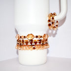 A collection of beaded bracelets in shades of brown and gold. The bracelets feature various bead shapes, including faceted beads and heart-shaped beads. Some bracelets are stacked together, while others are displayed separately.