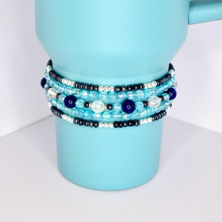 Handcrafted stack of tumbler bracelets with deep blue, turquoise, silver, and translucent beads, displayed on a two-tone tumbler.