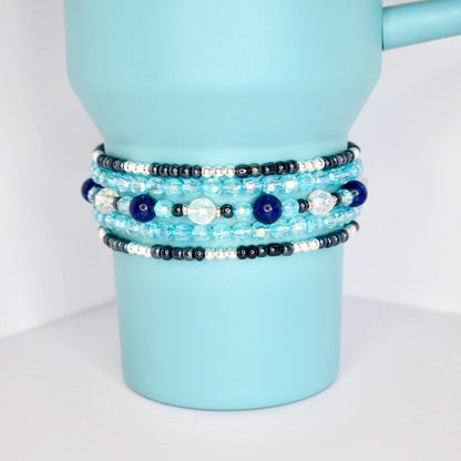 Blue and silver beaded tumbler bracelets wrapped around a metallic blue tumbler, showcasing layered textures and sparkle.
