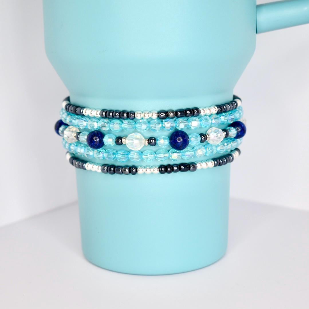 Blue and silver beaded tumbler bracelets wrapped around a metallic blue tumbler, showcasing layered textures and sparkle.