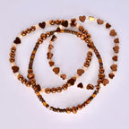 Three beaded bracelets in shades of brown and gold. The bracelets feature a mix of small round beads, heart-shaped beads, and crystal-like beads. The beads are strung together to create a layered effect, with the bracelets overlapping each other. The overall aesthetic is delicate and feminine.