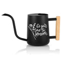 Black watering can with a long, curved spout and a wooden handle. The watering can features white script that reads 'it's your time to blossom' with a floral design. The handle is made of light-colored wood, and the spout is black.