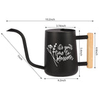 A black watering can with a long, curved spout and a wooden handle. The watering can has white text that reads 'it's your time to blossom' with a floral design. Dimensions are labeled: 10.2inch, 7inch, 4.2inch, 3.74inch, 5.4inch, and 4.4inch.