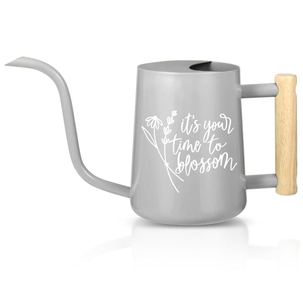 A gray watering can with a long, thin spout and a wooden handle. The watering can has a curved design and a white floral graphic with the words 'it's your time to blossom' printed on the side. The handle is made of light-colored wood.