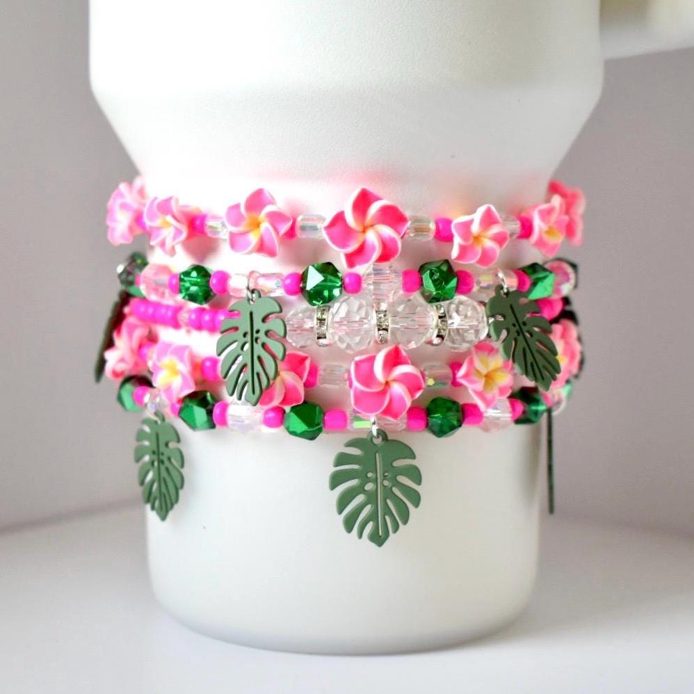 Tropical tumbler bracelet set with vibrant pink flowers, glittery green beads, and monstera charms—handmade stack of 5 ideal for customizing your favorite tumbler in paradise style.