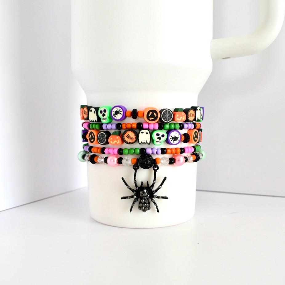Set of 5 beaded Halloween bracelets for tumbler cups with festive themed charms—skulls, jack-o’-lanterns, spiderwebs, ghosts, and rhinestone spider charm.
