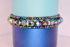 Colorful iridescent beaded tumbler bracelets with shiny metallic hues and rhinestone accents, wrapped around a two-tone blue tumbler.
