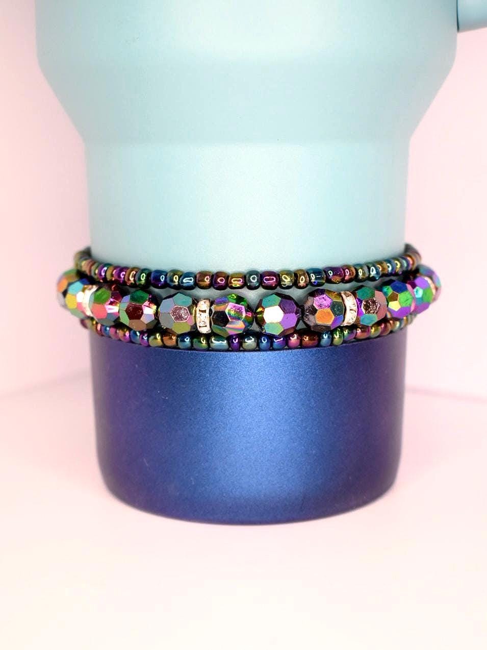 Stack of 3 iridescent tumbler bracelets with multicolor faceted beads and metallic seed beads, shown on a blue gradient tumbler for a bold, reflective style.