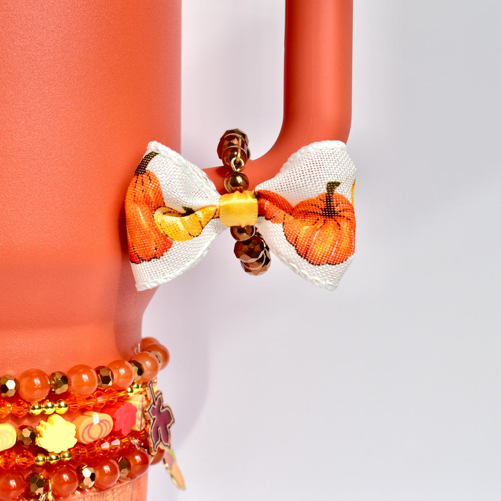 Fall tumbler handle bracelet made of glossy bronze and gold beads, accented with a mini bow showcasing an autumn pumpkin print, attached to a coral Stanley tumbler handle.
