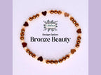 Bronze Beauty bracelet. The bracelet features a circular design with alternating bronze-colored beads and heart-shaped charms. The beads are a mix of bronze and cream colors. The bracelet is displayed on a white surface, with the words 'Design Option: Bronze Beauty' in black text.