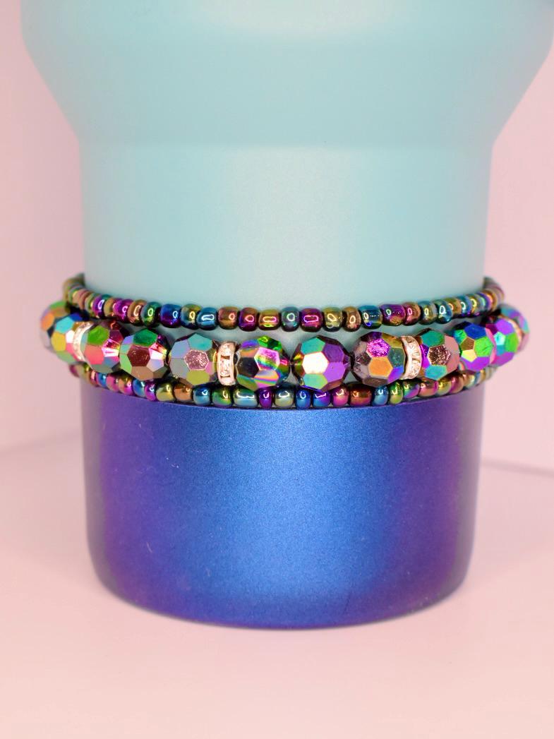 Set of 3 rainbow-toned tumbler bracelets featuring faceted glass beads and reflective metallic details, styled on a modern blue ombre tumbler.