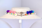 Two colorful beaded necklaces displayed on a white surface. The top necklace features purple, pink, and white beads with a daisy charm. The bottom necklace has blue, green, orange, and pink beads. Both necklaces have silver clasps.