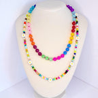 A colorful beaded necklace with a rainbow color scheme. The necklace features large, round beads in various colors, including blue, green, pink, orange, and purple. Smaller beads and white daisy accents are interspersed throughout the design, creating a playful and vibrant accessory.
