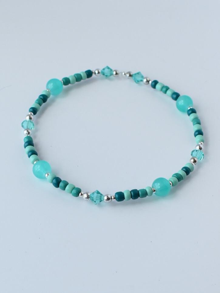 A beaded bracelet featuring turquoise and teal beads, interspersed with silver-colored accents. The bracelet has a mix of round and faceted beads, creating a delicate and colorful accessory.